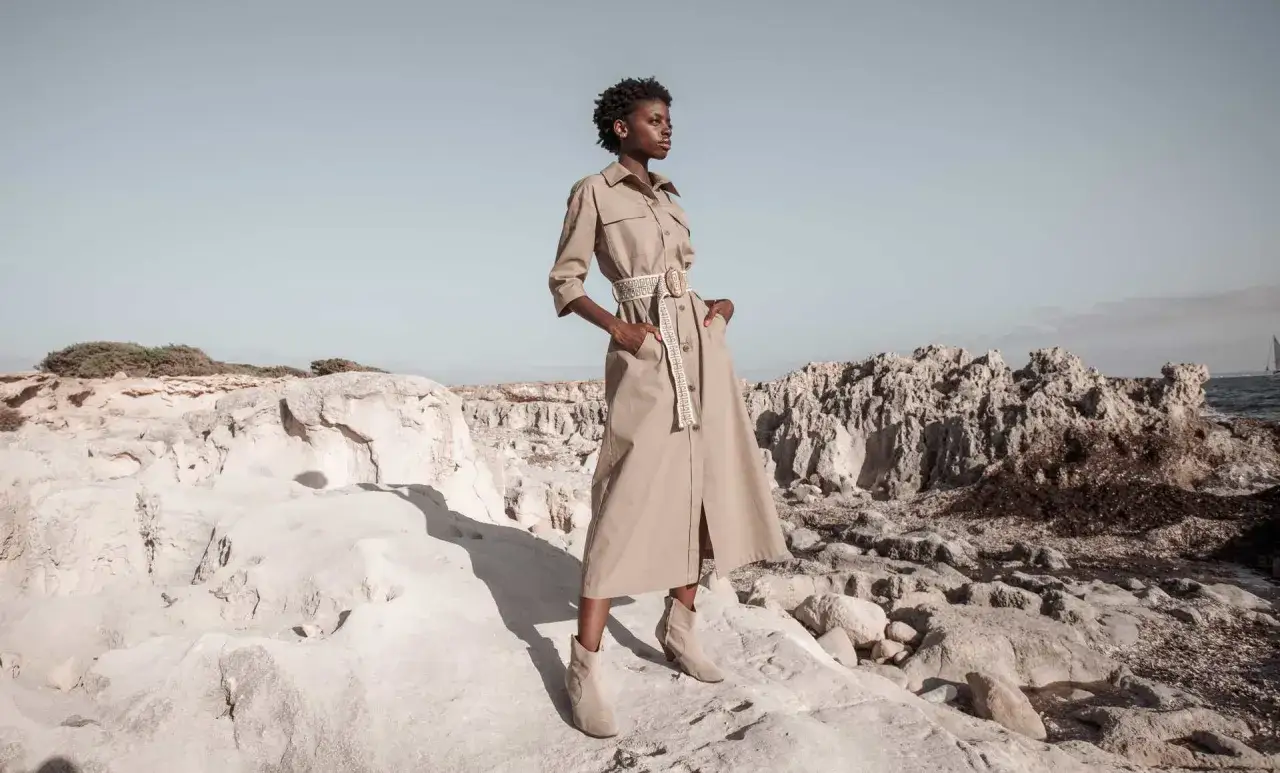 Frauenkleid im Safari-Stil, das die Werte von slow fashion verk&ouml;rpert. Steht auf felsigem Untergrund am Meer.