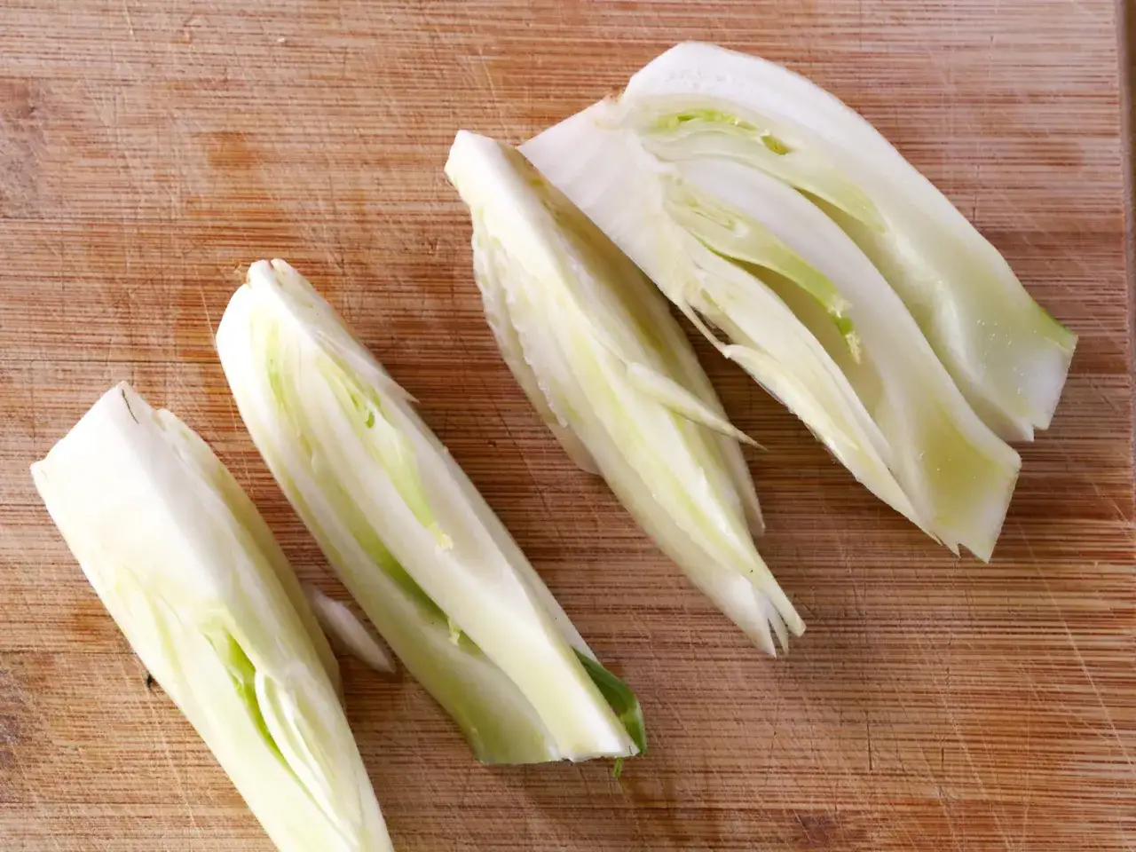 Vier geviertelte Fenchelknollen liegen auf einem Holzbrett. Perfekt, um Fenchel roh zu essen!