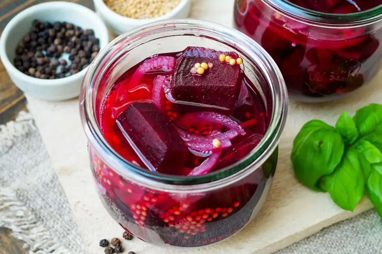 Rote Bete haltbar machen: Ein Glas mit eingelegter Rote Bete, Zwiebeln und Senfkörnern. Daneben Schüsseln mit Pfeffer und Senfkörnern.