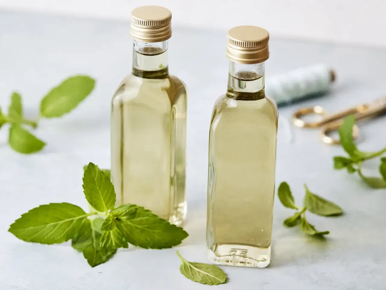 Zwei Flaschen mit selbstgemachtem Minzsirup, umgeben von frischen Minzbl&auml;ttern. Ein Hauch von DIY-Frische!