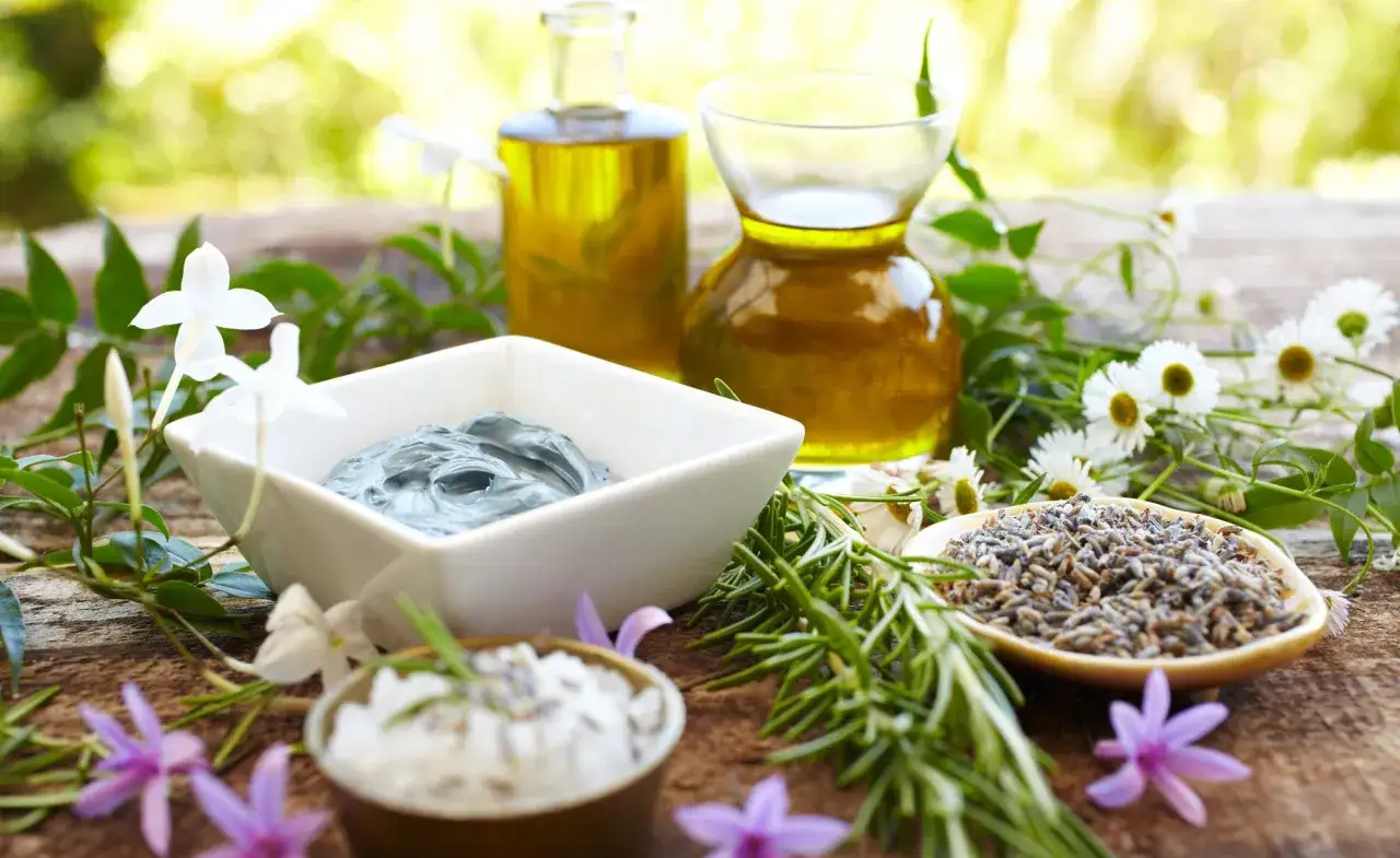 Zutaten für kosmetik selber machen: Tonmaske, Lavendel, Kräuter und Öle auf Holztisch.