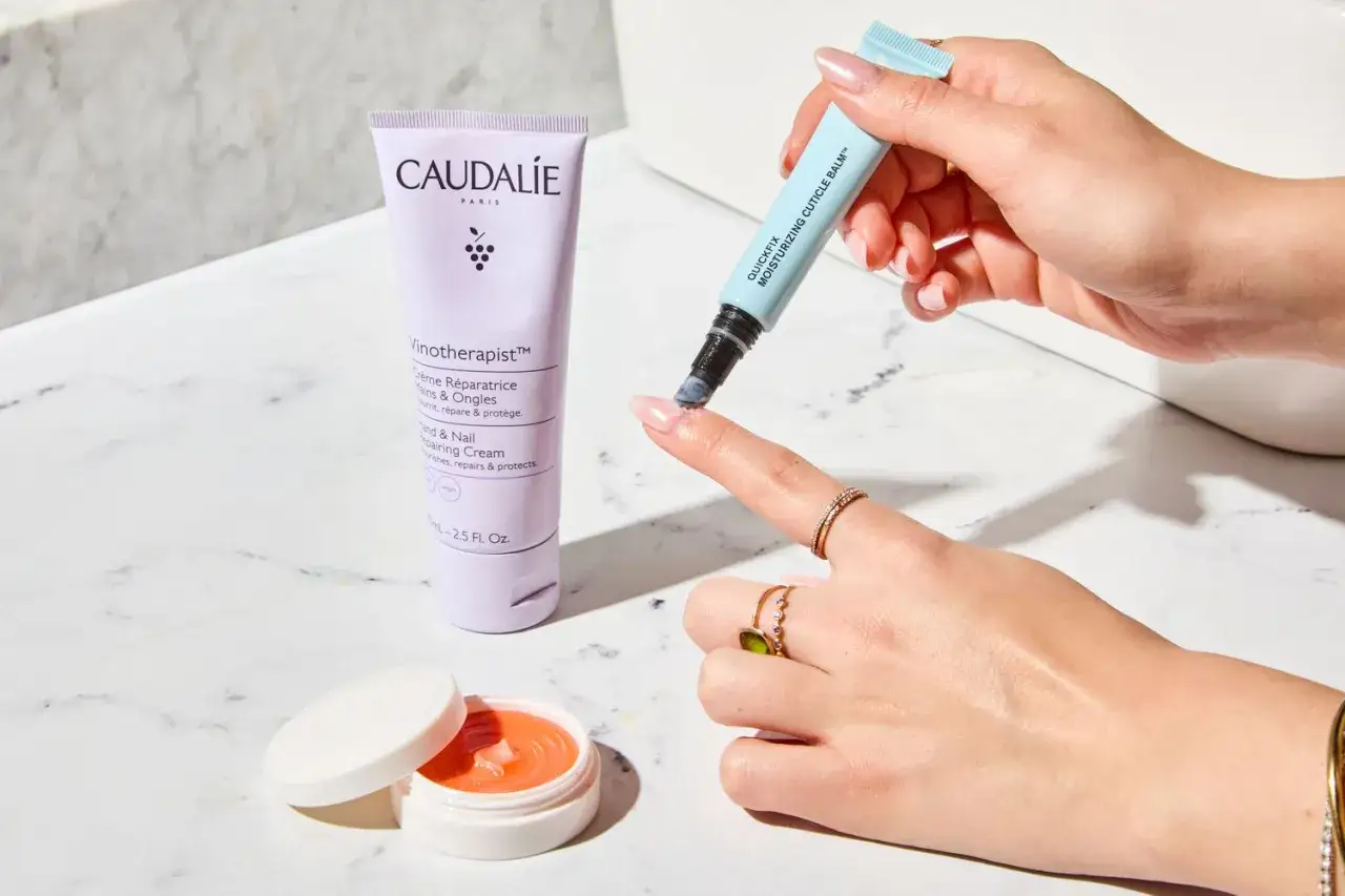H&auml;nde mit trockener Nagelhaut werden mit einem feuchtigkeitsspendenden Nagelhautbalsam gepflegt. Daneben eine Handcreme von Caudalie.
