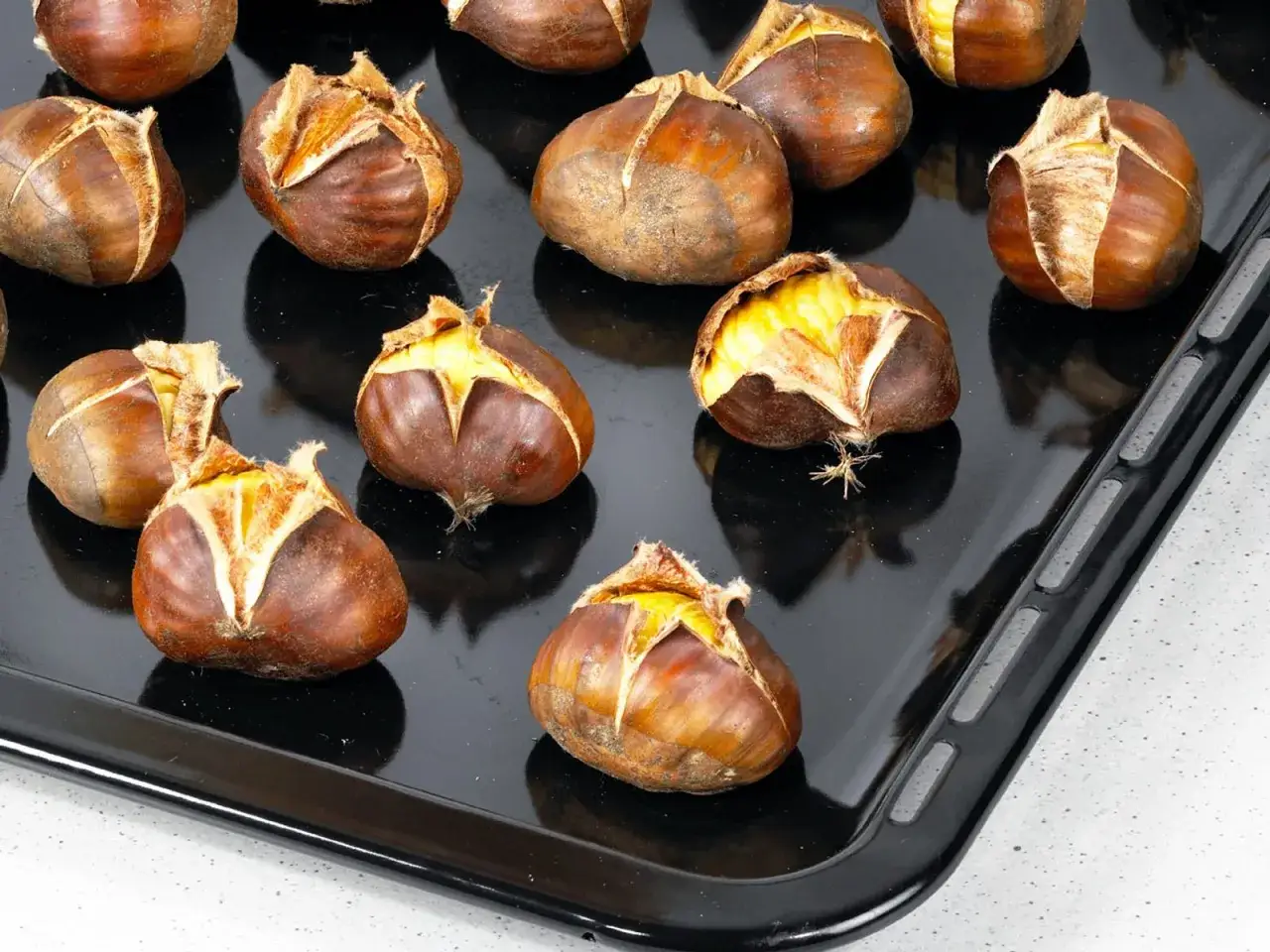 Ger&ouml;stete Maronen auf einem Backblech, bereit f&uuml;r die Maronen Zubereitung. Die Schale ist eingeschnitten und leicht ge&ouml;ffnet, was das k&ouml;stliche Innere zeigt.