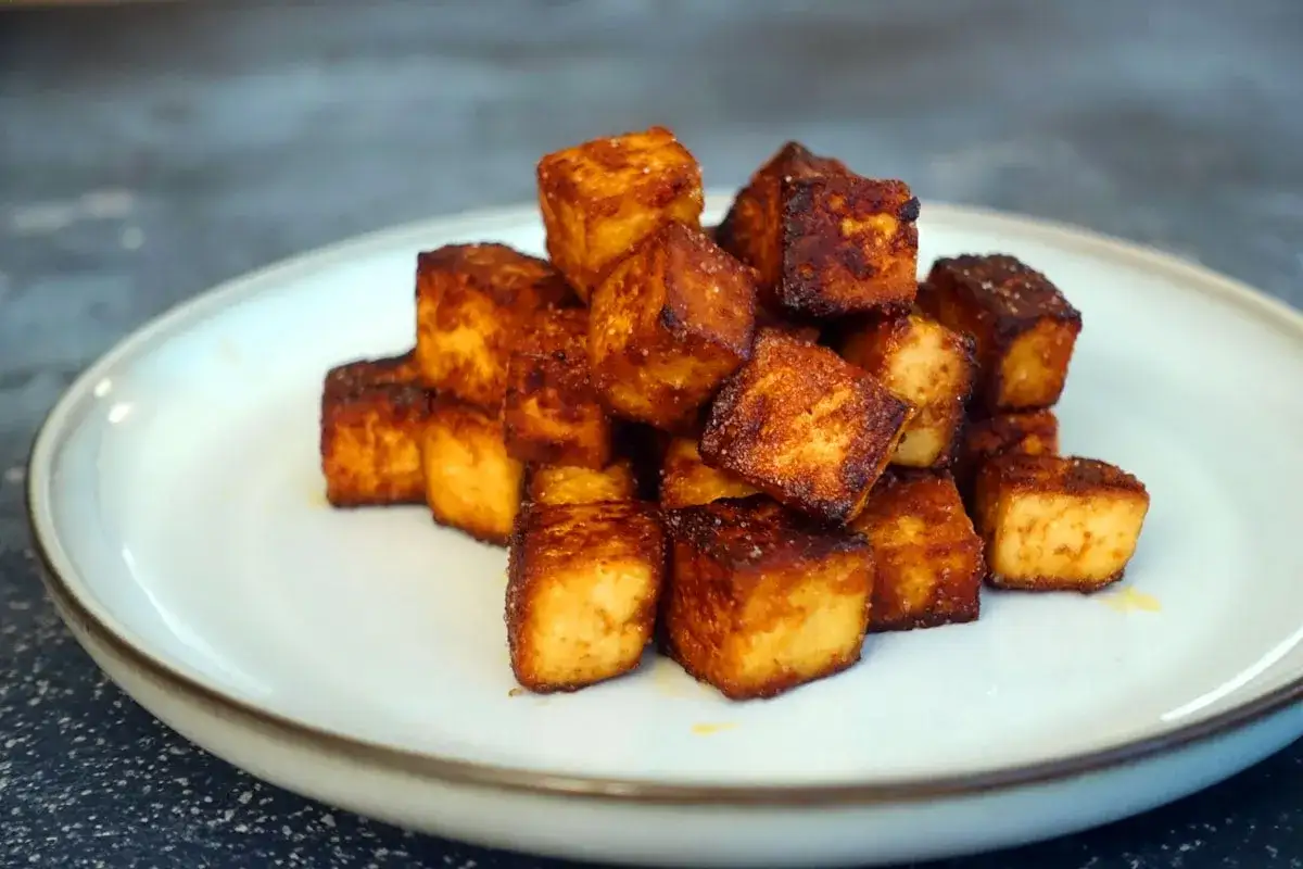Goldbraun gebratene Tofuw&uuml;rfel, perfekt zum tofu zubereiten. Sie liegen auf einem Teller und sehen knusprig aus.