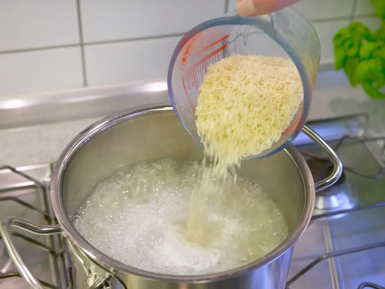 Reis wird aus einem Messbecher in einen Topf mit kochendem Wasser gesch&uuml;ttet. So einfach ist naturreis kochen.