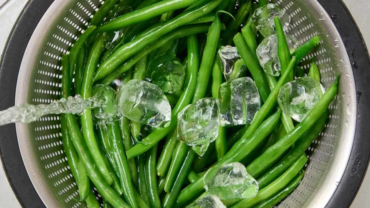 Grüne Bohnen werden in einem Sieb mit Eiswasser abgeschreckt, um das Bohnen blanchieren zu stoppen und ihre Farbe zu erhalten.