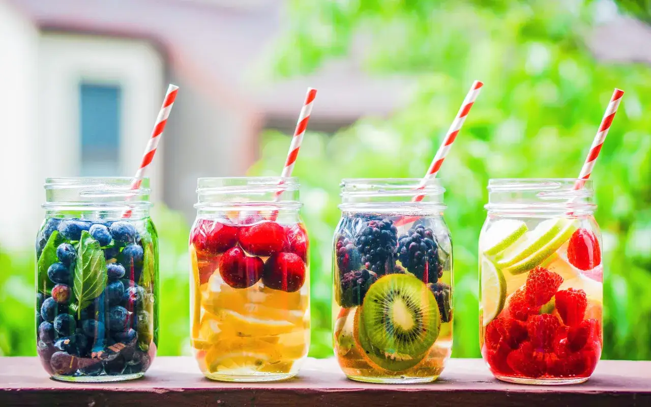 Vier Gläser mit Früchten und Strohhalmen: Blaubeeren, Kirschen, Brombeeren mit Kiwi, Himbeeren mit Limette. Perfekt, um bei Hitze etwas Frisches zu kochen.