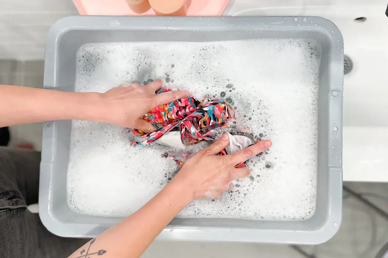 Hände waschen ein buntes bikini in schaumigem Wasser.