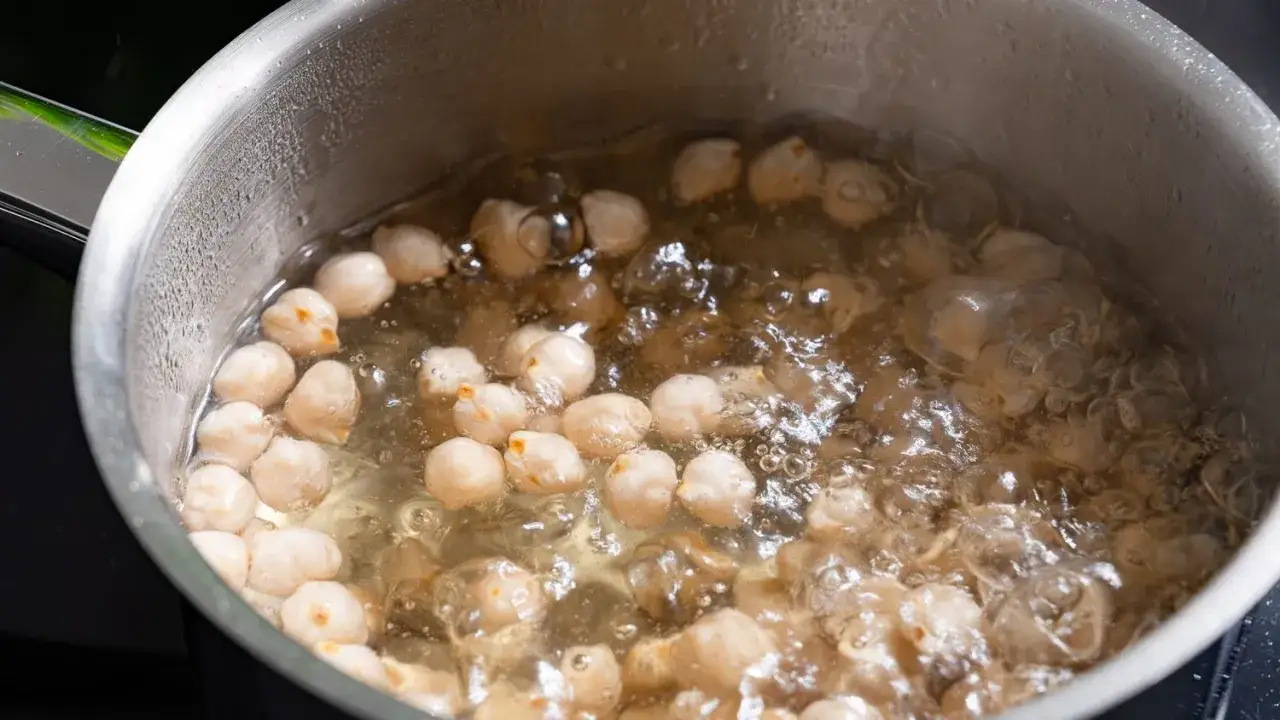 Kichererbsen kochen in einem Topf. Das Wasser sprudelt und die Kichererbsen werden weich.