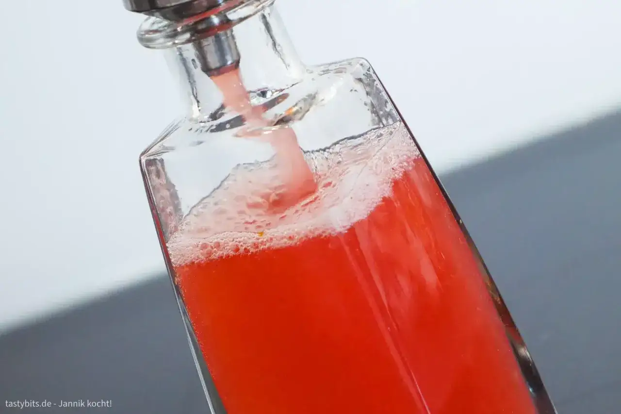 Frisch zubereiteter Rhabarbersirup flie&szlig;t sch&auml;umend in eine Glasflasche. So einfach l&auml;sst sich Rhabarbersirup selber machen!