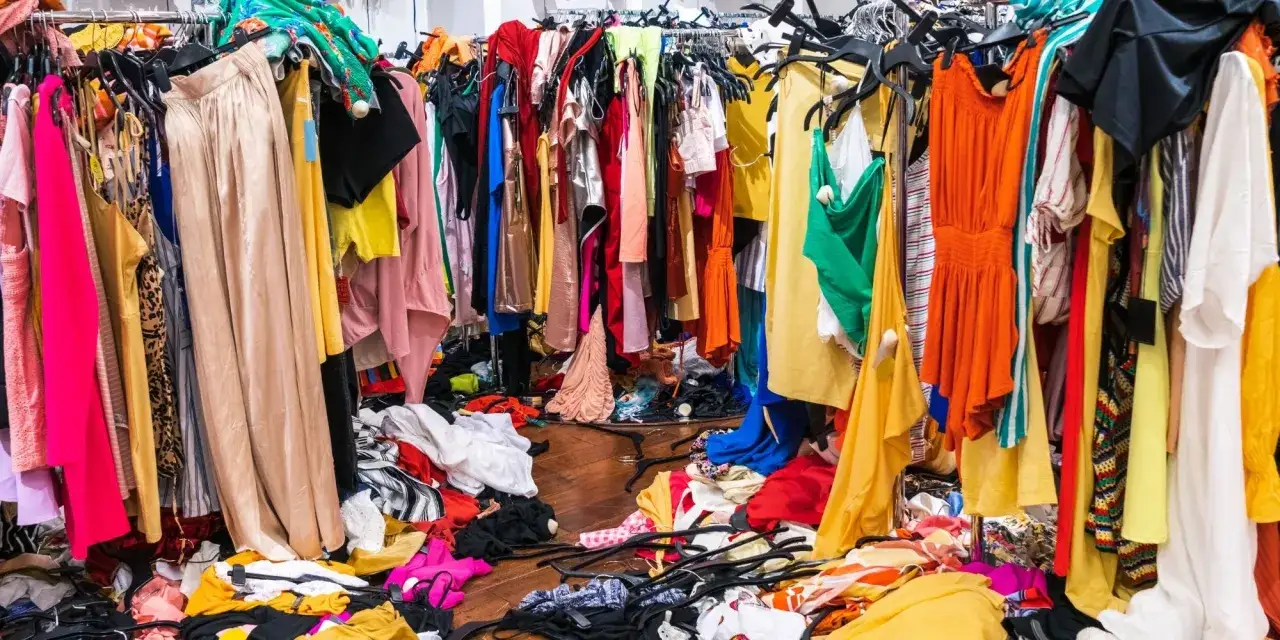 Bunte Kleider auf Kleiderstangen und auf dem Boden. Die Vielfalt zeigt die schnellen fast fashion vorteile: st&auml;ndig neue Trends f&uuml;r jeden Geldbeutel.