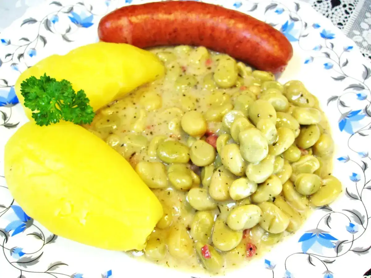 Dicke Bohnen zubereiten: Ein Teller mit deftigen dicken Bohnen in cremiger Sauce, dazu Salzkartoffeln und eine herzhafte Wurst.
