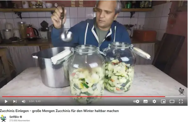 Mann füllt mit Schöpfkelle klein geschnittene Zucchini in Einmachgläser. Zucchini einwecken für den Winter.