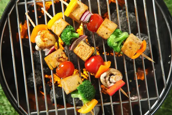 Vegane Grillrezepte: Bunte Gemüsespieße mit Tofu, Paprika, Brokkoli und Tomaten brutzeln auf dem Grill über glühender Kohle.