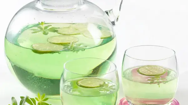Erfrischendes Getränk mit Limettenscheiben und Waldmeister-Zweigen in einer Karaffe und Gläsern. Perfekt für Waldmeister Rezepte.