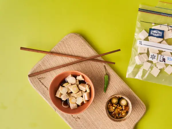 Vorbereitung für tofu einfrieren: gewürfelter Tofu in Schüssel mit Soße, daneben ein kleiner Chili und ein Beutel mit gefrorenem Tofu.