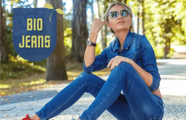 Frau in Jeansjacke und Hose, die entspannt im Park sitzt. "BIO JEANS" Schriftzug deutet auf nachhaltige deutsche Jeansmarken hin.