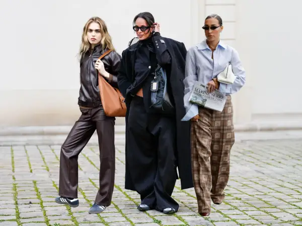 Drei Frauen in modischer Kleidung, die zeigt, was bedeutet nachhaltige Kleidung: Leder, Oversize-Schnitte und karierte Hosen.