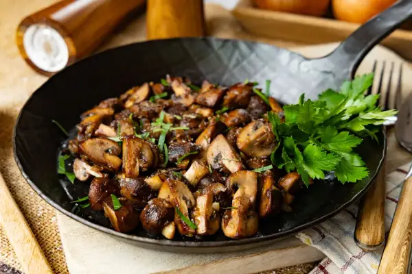 Gebratene Champignons mit Petersilie in einer Pfanne, perfekt zubereitet.