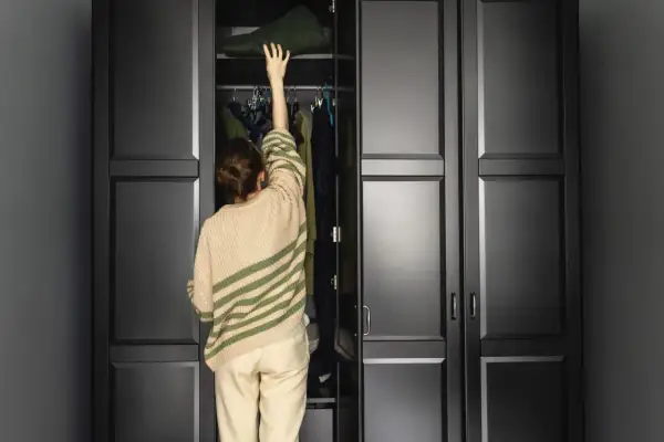 Frau räumt Kleidung in einen dunklen Kleiderschrank. Hoffentlich riecht der Kleiderschrank bald nicht mehr muffig.
