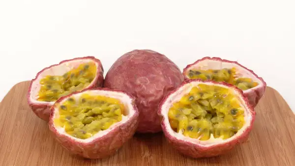 Ein ganzes und drei halbierte Passionsfrüchte liegen auf einem Holzbrett. Das Fruchtfleisch mit den Kernen lädt zum Passionsfrucht essen ein.