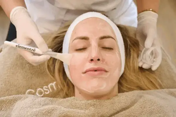 Eine Kosmetikerin trägt mit einem Pinsel eine Maske auf das Gesicht einer Frau auf, um es zu reinigen.