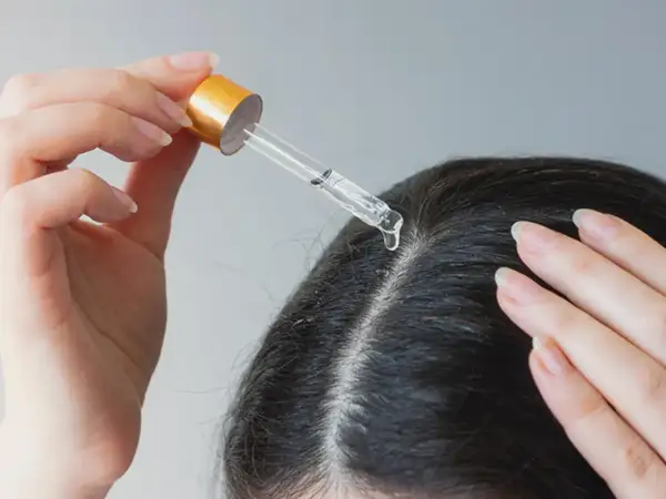 Eine Hand trägt mit einer Pipette ein Öl auf die Kopfhaut auf. Ein natürliches hausmittel gegen schuppen und juckende kopfhaut.