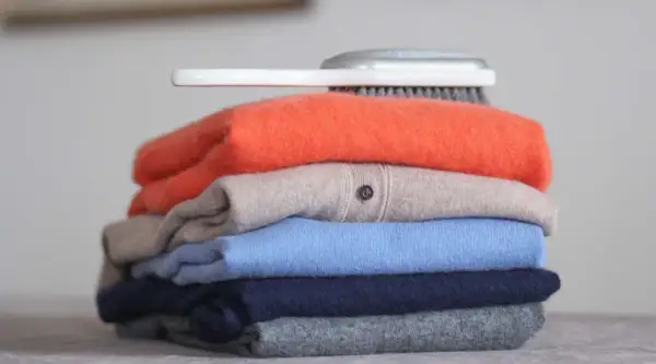Ein Stapel bunter Pullover, was ist Kaschmir? Weiche, luxuriöse Kleidung, die Pflege braucht. Ein Bürstchen liegt obenauf.
