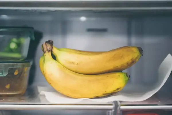 Ein Bund reifer Bananen liegt auf einem Küchentuch im Kühlschrank. So lassen sich Bananen lagern, um sie länger frisch zu halten.