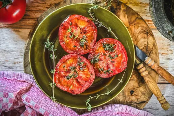 Drei saftige Scheiben Tomaten, perfekt gegrillt und mit frischen Kräutern bestreut, liegen auf einem grünen Teller. Ein Genuss für alle Sinne!