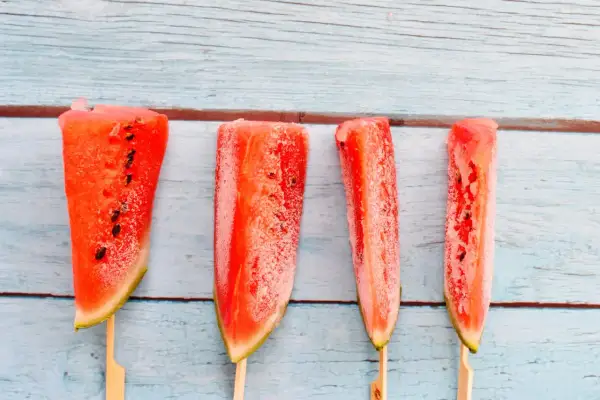 Vier gefrorene Wassermelonenstücke auf Holzstäbchen. Man kann Wassermelone einfrieren und so erfrischende Snacks für heiße Tage kreieren.