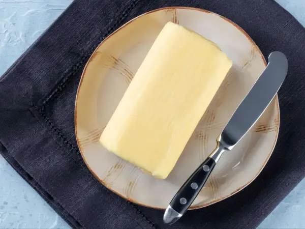 Ein Block Butter auf einem Teller mit einem Messer daneben. Die Frage, wie lange ist Butter haltbar, beschäftigt viele.