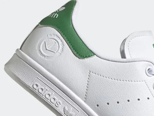 Detailaufnahme eines weißen Adidas Stan Smith Schuhs mit grünen Akzenten. Das vegane Siegel ist gut sichtbar. Perfekt für leichte, vegane Sommerschuhe.