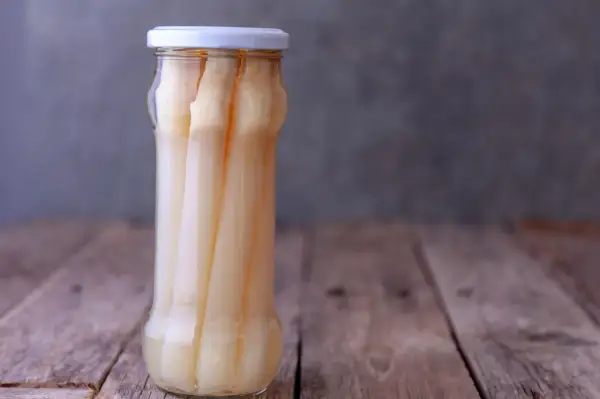 Ein Glas mit eingelegtem weißen Spargel steht auf einem Holztisch. Perfekt für das Spargel einkochen.